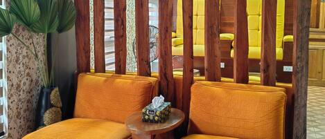 A seating area with two yellow cushioned chairs, a small round table with a tissue box, and a decorative wooden partition.