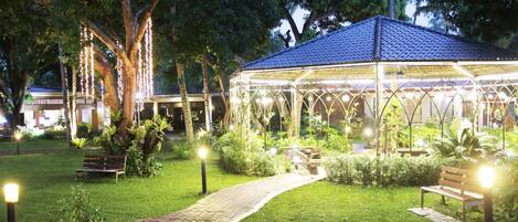 A gazebo with a tiled roof, surrounded by a paved walkway, benches, and potted plants.