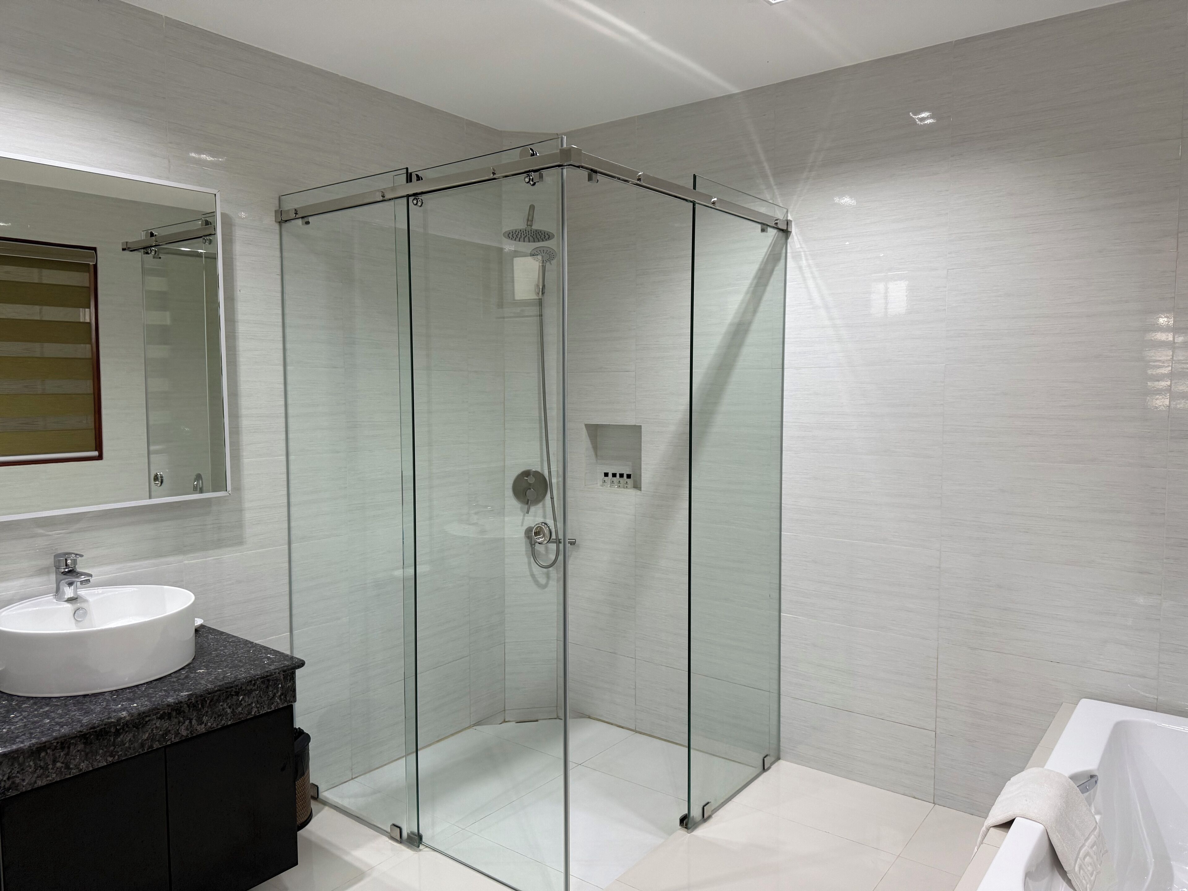 A modern bathroom with a glass-enclosed shower, a sink with a dark countertop, and a white bathtub.