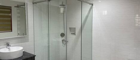 A modern bathroom with a glass-enclosed shower, a sink with a dark countertop, and a white bathtub.