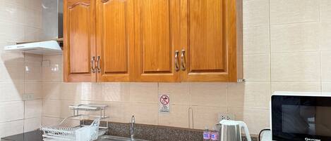 A kitchen with wooden cabinets, a stainless steel sink, a microwave, and a kettle.