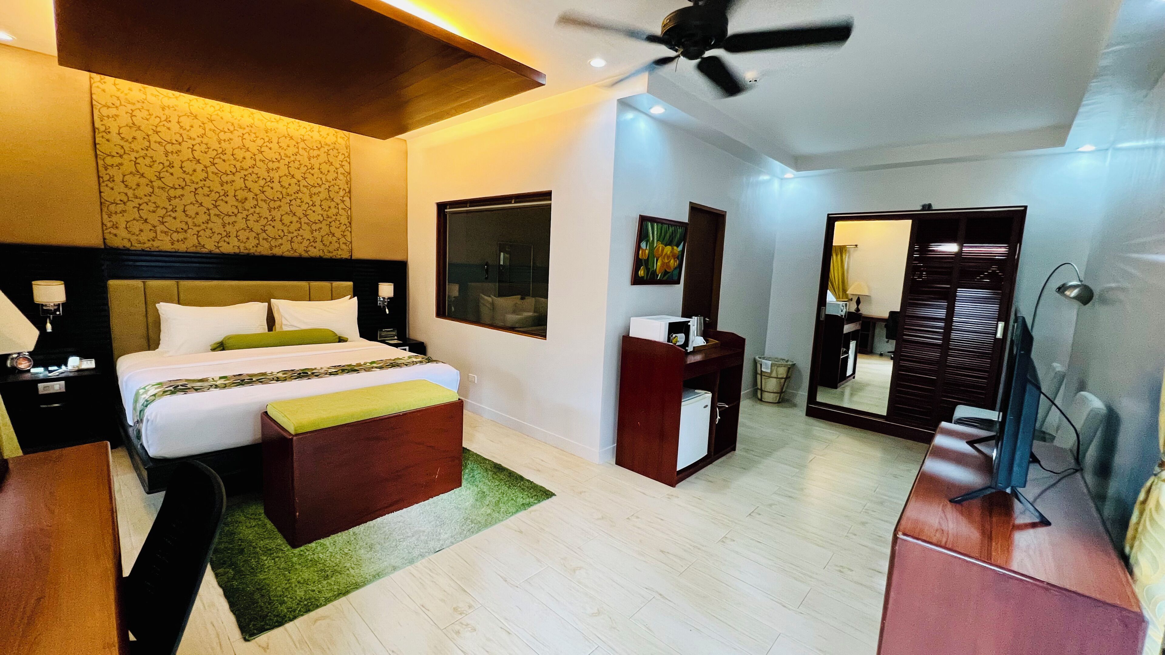 A hotel room with a bed, bedside table, nightstand, desk, chair, mirror, and ceiling fan.