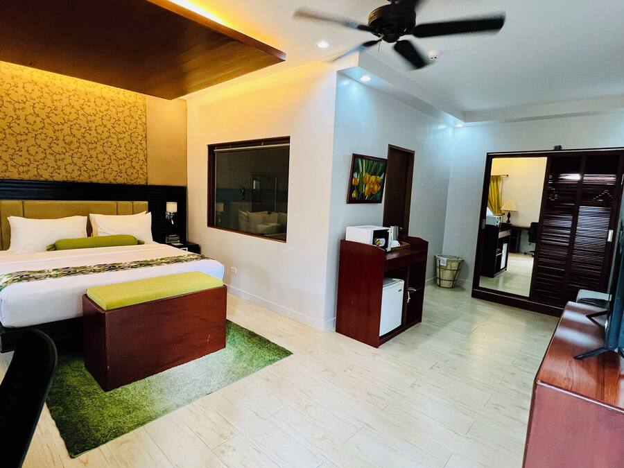 Quarto de hotel com cama, mesa de cabeceira, escrivaninha, cadeira, espelho e ventoinha no teto.