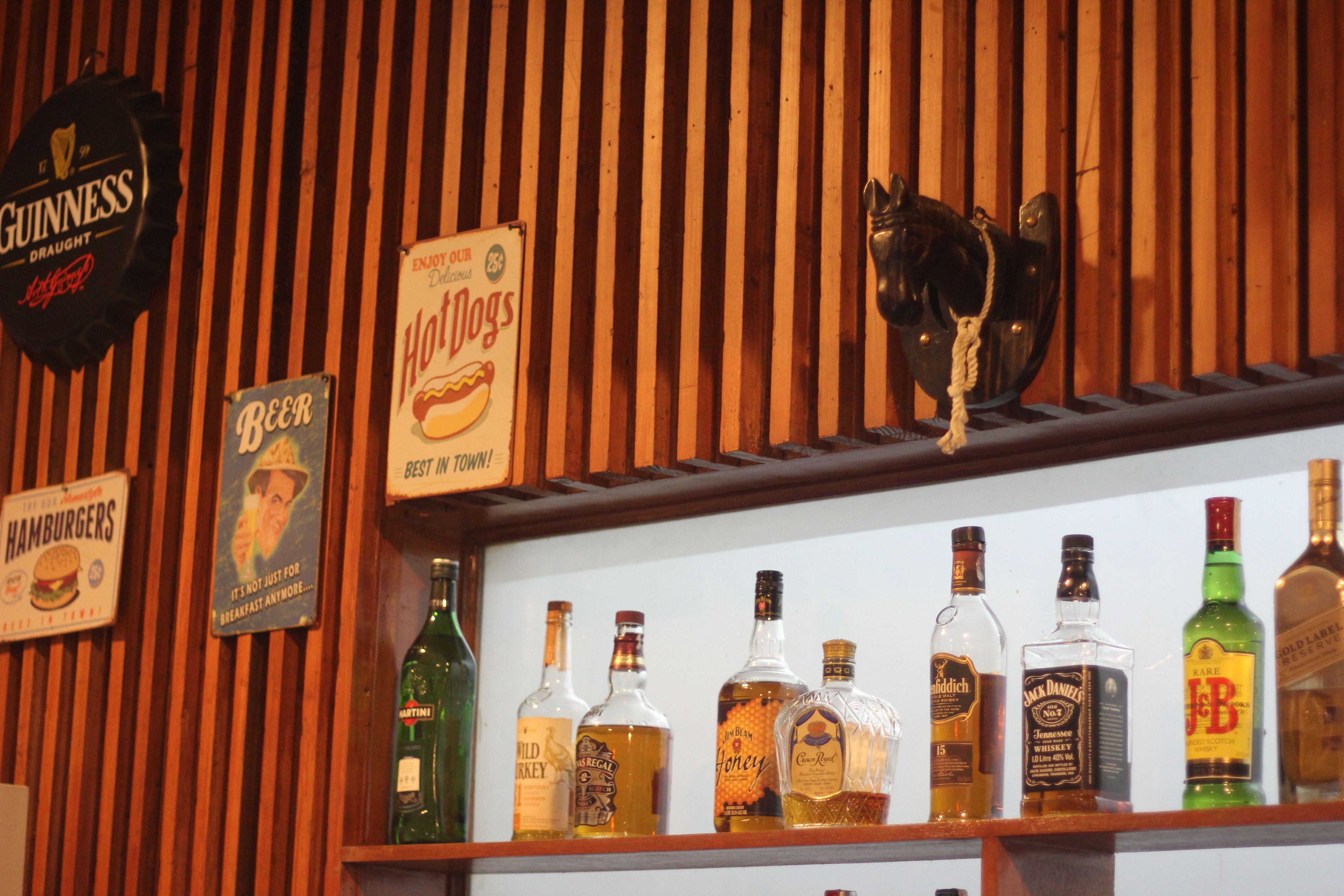 Una zona de bar con listones de madera, un letrero de Guinness, un anuncio de perritos calientes y varias botellas de licor.