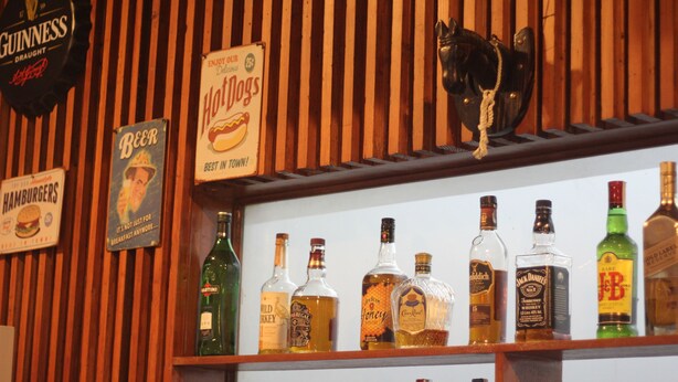 A bar area with wooden slats, a Guinness sign, a sign for hot dogs, and various liquor bottles. - Batangas Country Club (Batangas City)