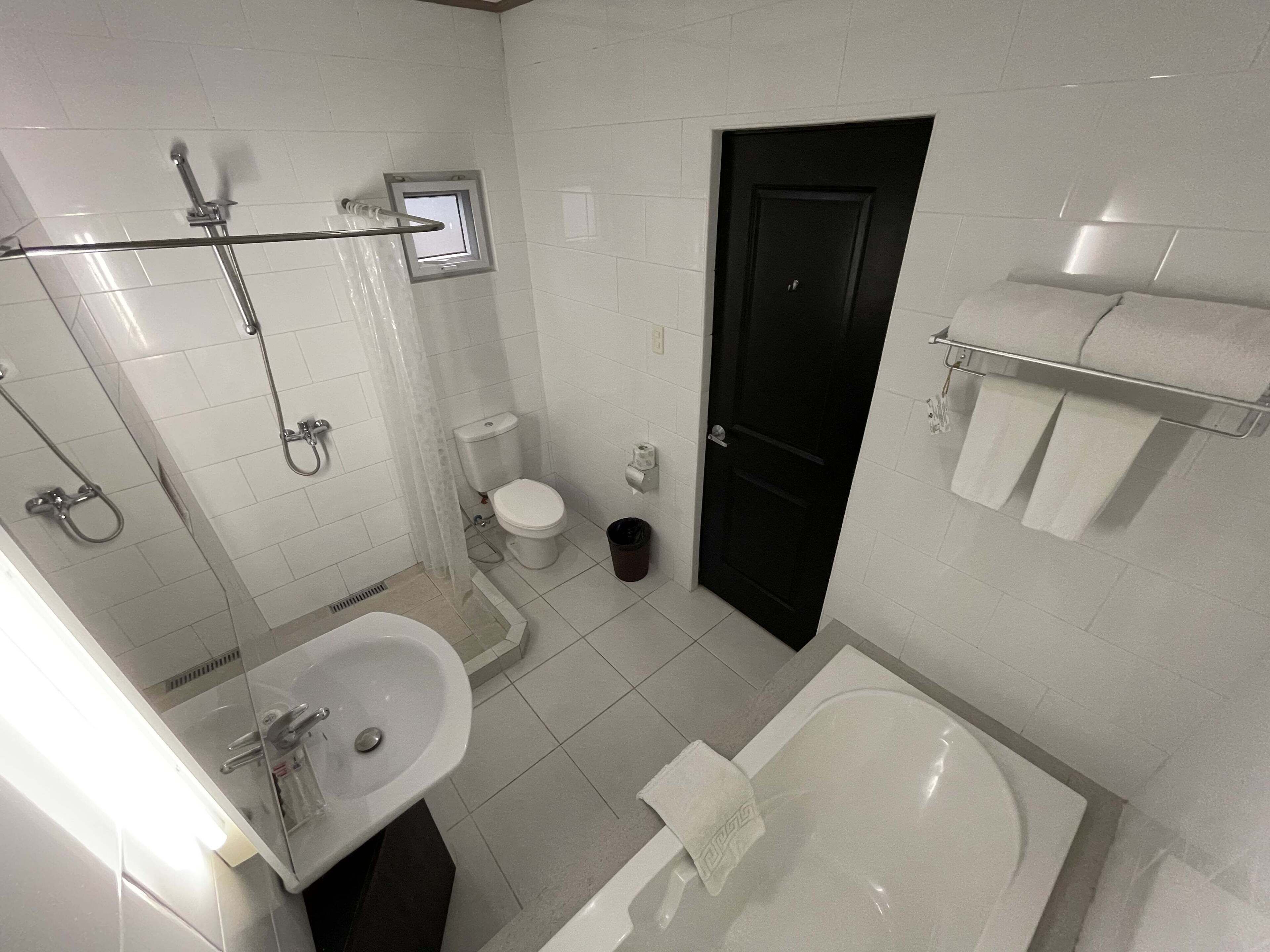 A bathroom with a bathtub, a sink, a toilet, a shower, and a black door.