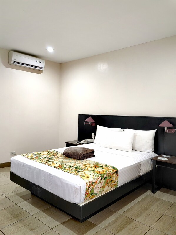 A hotel room with a bed, a nightstand, a lamp, and an air conditioning unit. - Batangas Country Club (Batangas City)
