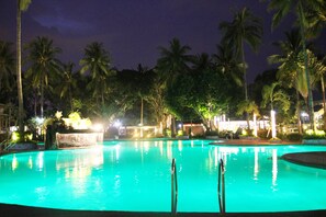 A nighttime view of a swimming pool surrounded by palm trees and illuminated by ambient lighting. - Batangas Country Club (Batangas City)