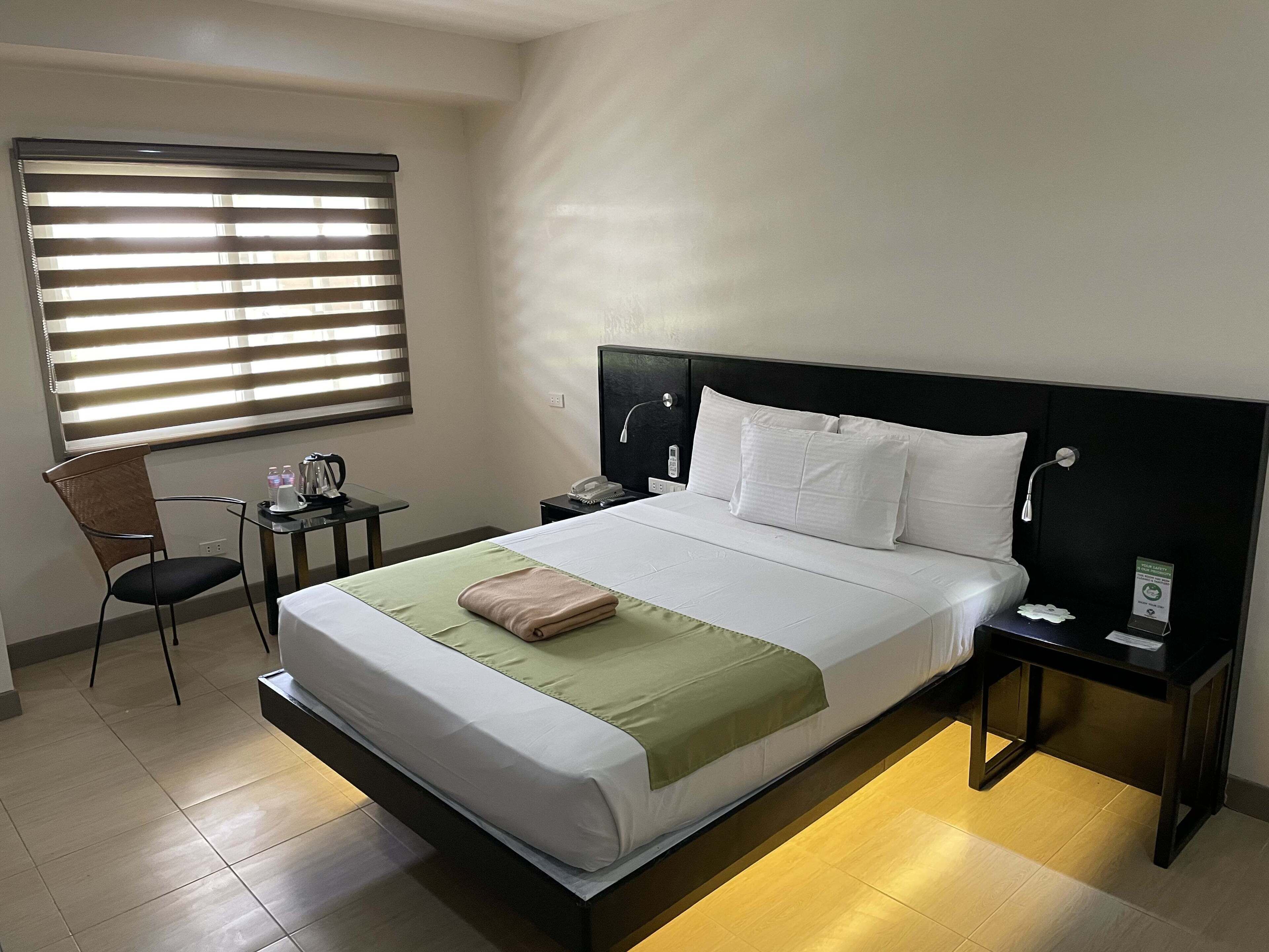 Habitación de hotel con una cama grande, una mesita de noche, una silla, un escritorio y una ventana con persianas.
