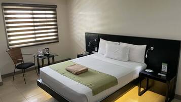 Habitación de hotel con una cama grande, una mesita de noche, una silla, un escritorio y una ventana con persianas.