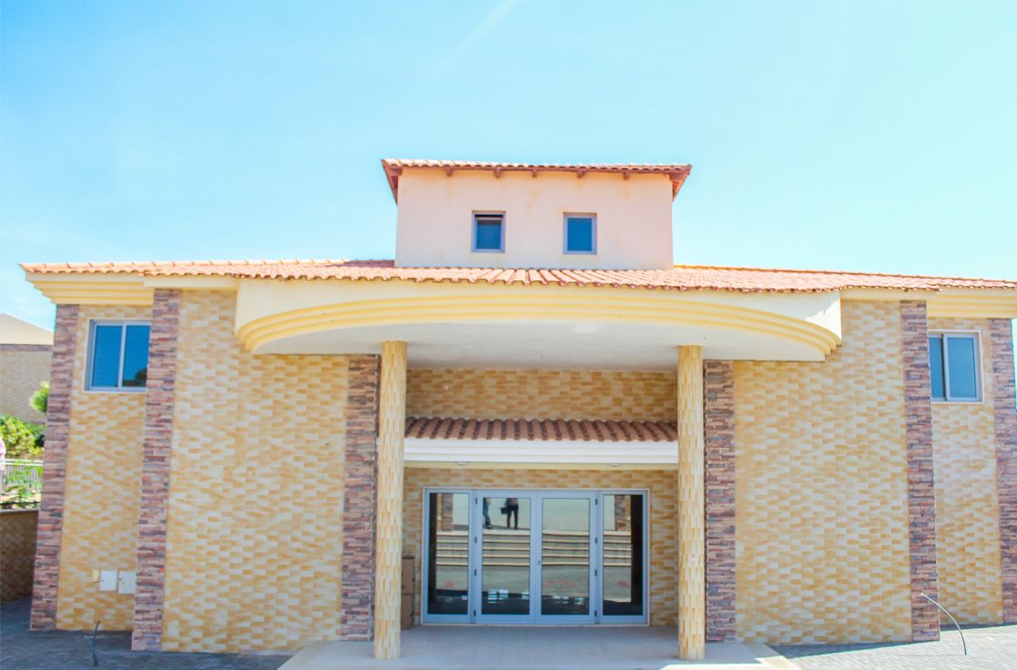 A two-story building with a tiled roof, a central entrance with glass doors, and a small balcony on the upper floor.