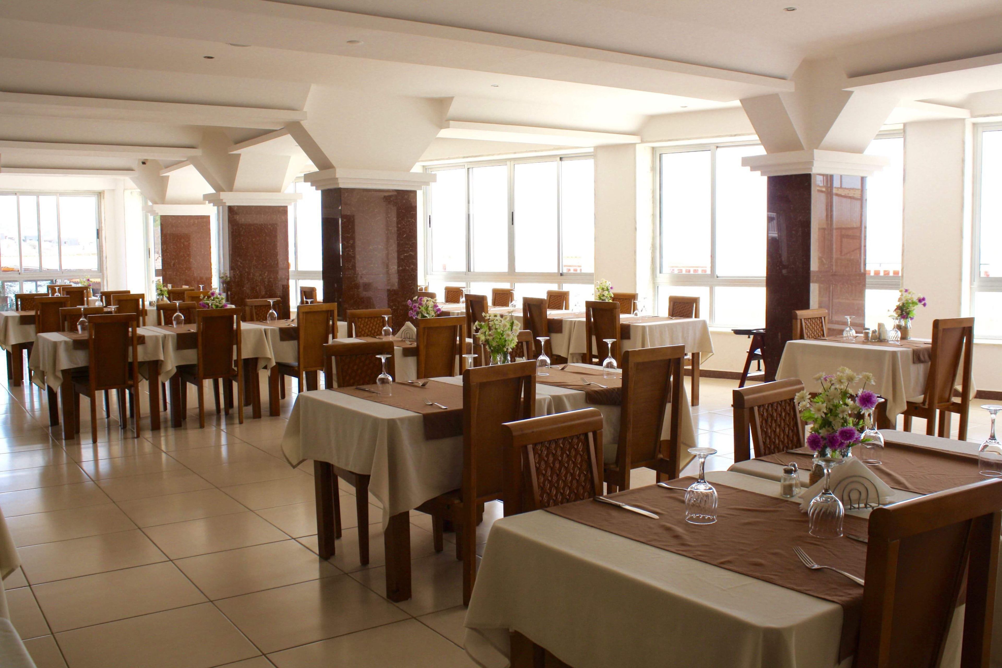 Un vaste espace dédié à la salle à manger, avec de nombreuses tables et chaises, de grandes fenêtres et un aménagement propre et moderne.