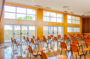 A spacious room with large windows, wooden walls, and rows of orange chairs arranged for seating. - Hotel Vulcão (Cidade Velha)