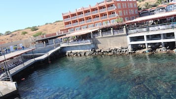 Ein Gebäude am Wasserufer mit Balkonen, einer Pier, die ins Wasser ragt, und einer felsigen Küstenlinie.