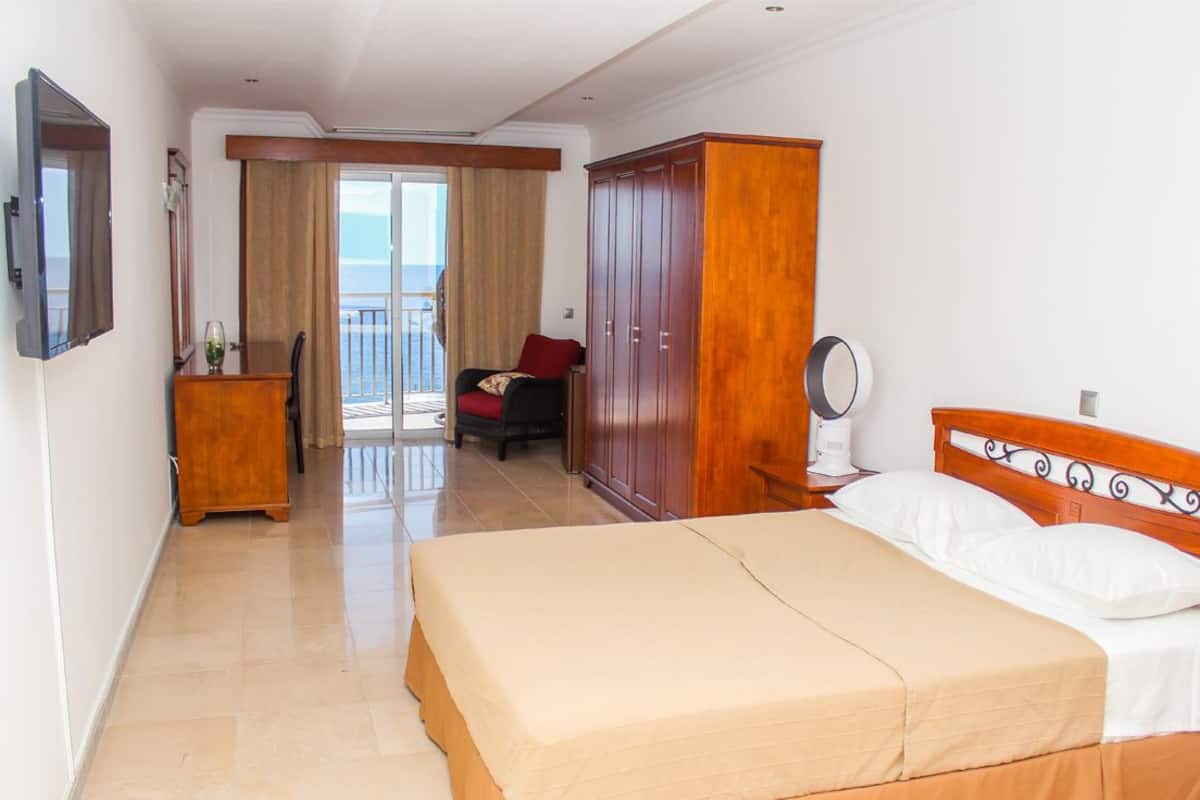 A hotel room with a bed, wardrobe, bedside table, and a view of the balcony.