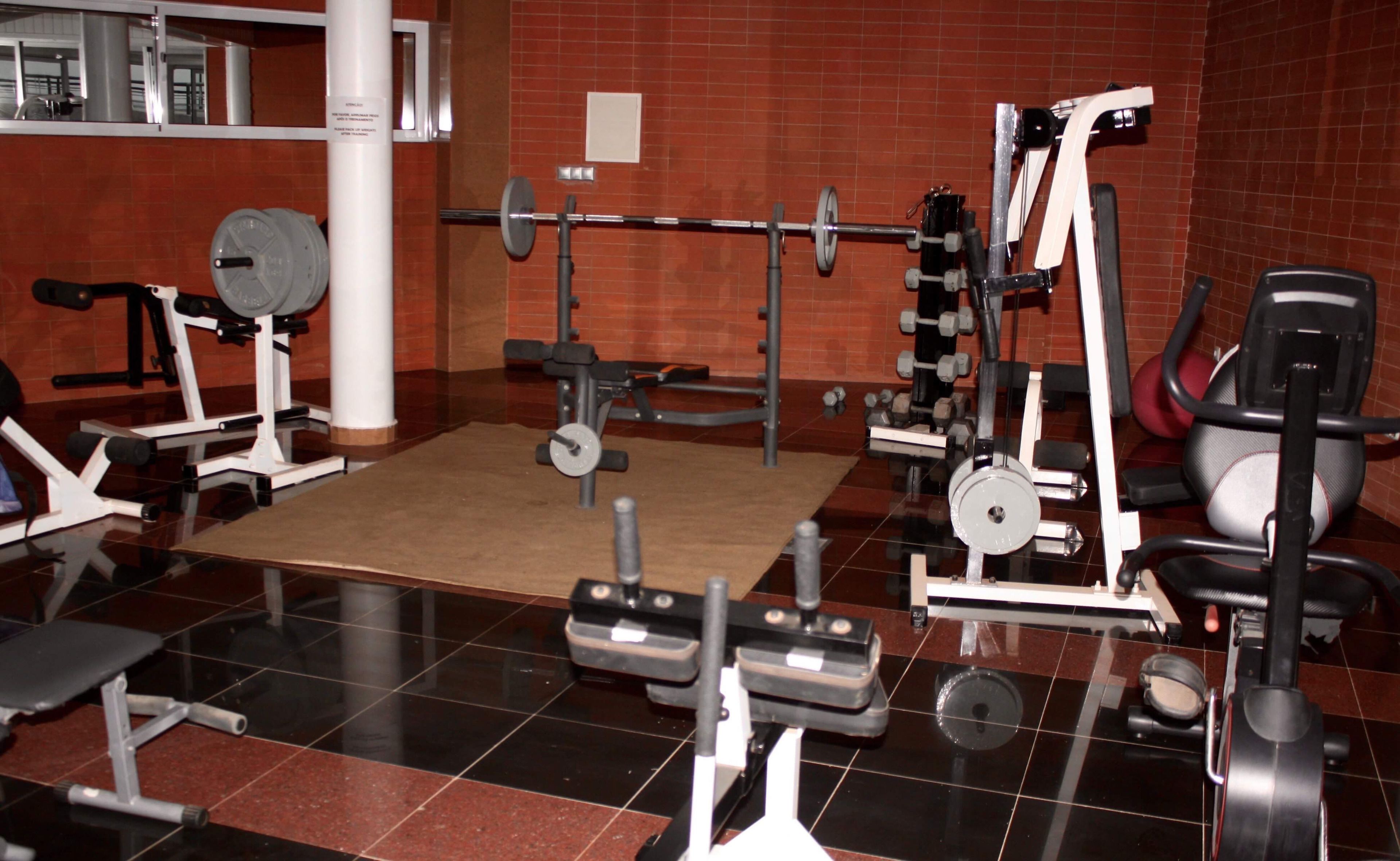 Une salle de sport équipée de divers appareils d’entraînement, notamment un banc de développé couché, un support à squats et des haltères.