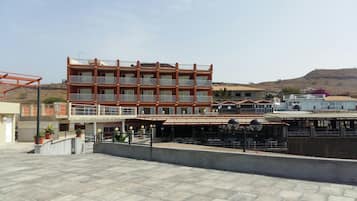 Un hotel de varios pisos con balcones, mobiliario exterior y vistas a un paisaje montañoso.