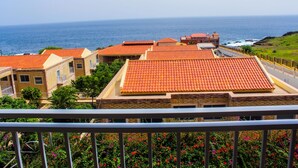 A coastal residential area with terracotta-roofed houses, a clear view of the ocean, and a balcony with a metal railing. - Hotel Vulcão (Cidade Velha)