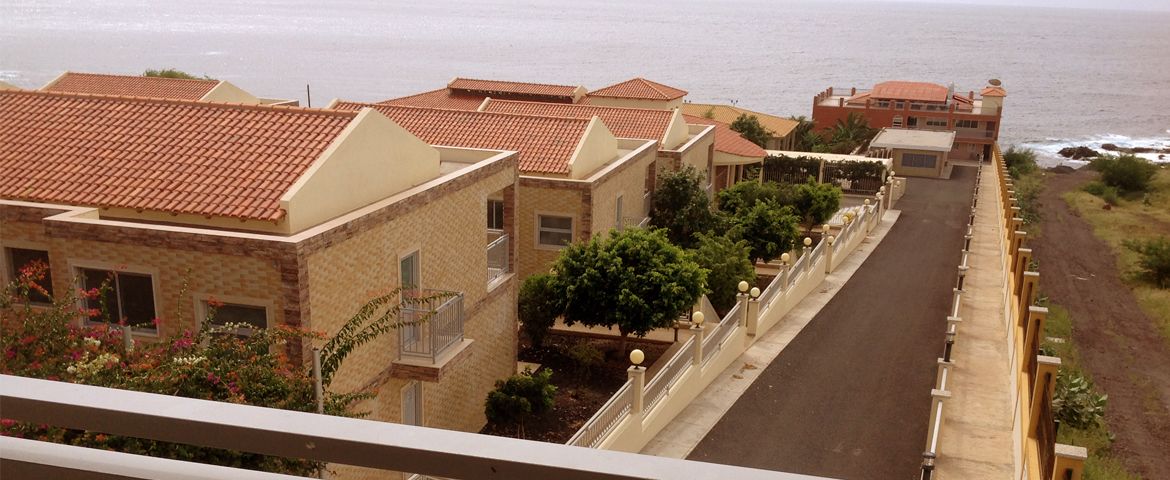 Un área residencial costera con casas escalonadas, una calle pavimentada y vista al mar.