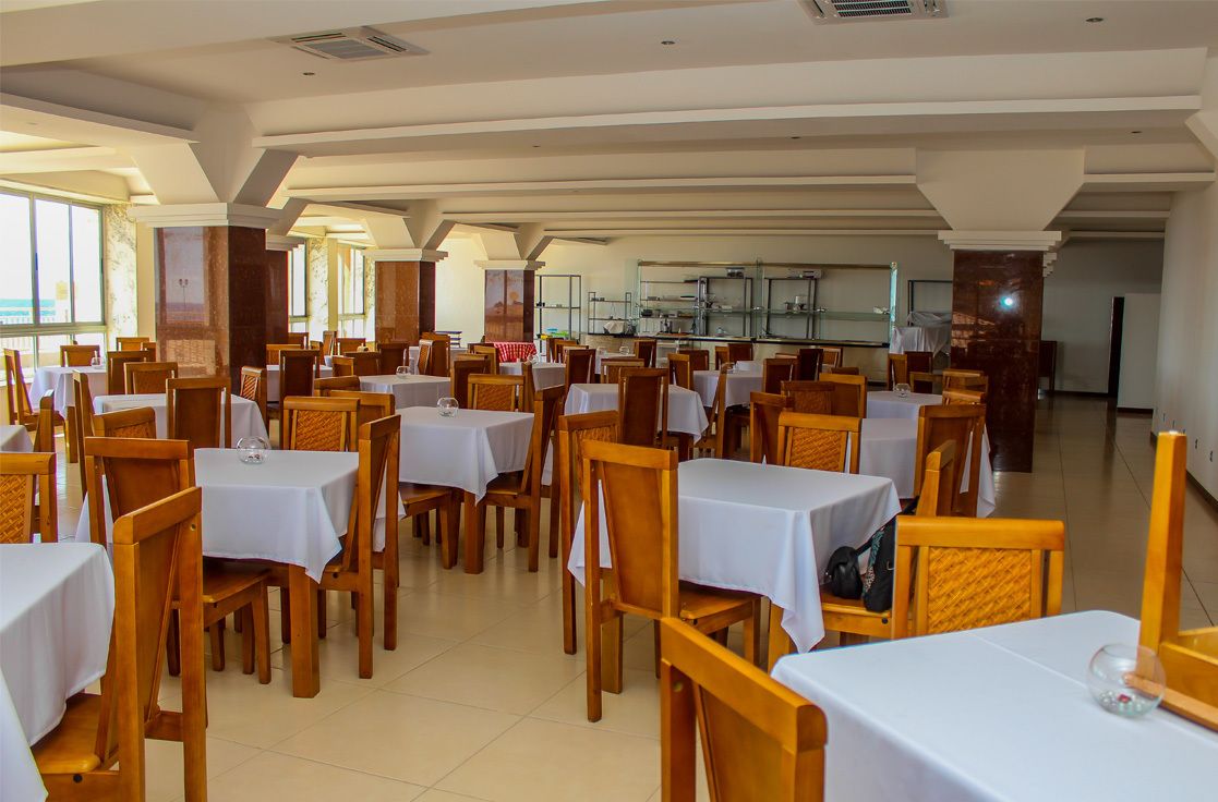 Un comedor amplio con varias mesas y sillas, ventanas grandes y una cocina al fondo.