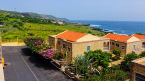 A coastal residential area with houses having red-tiled roofs, a paved road, and a view of the ocean. - Hotel Vulcão (Cidade Velha)