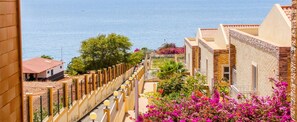 A coastal hotel with balconies overlooking the sea, a garden with pink flowers, and a view of the ocean. - Hotel Vulcão (Cidade Velha)