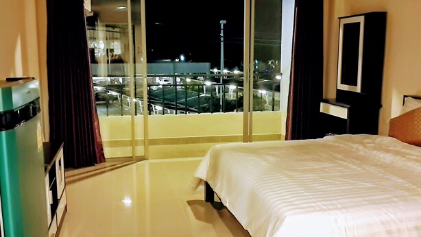 A hotel room with a bed, a minibar, a TV, and a balcony with a view of the city at night. - Santa Place (Pattaya)