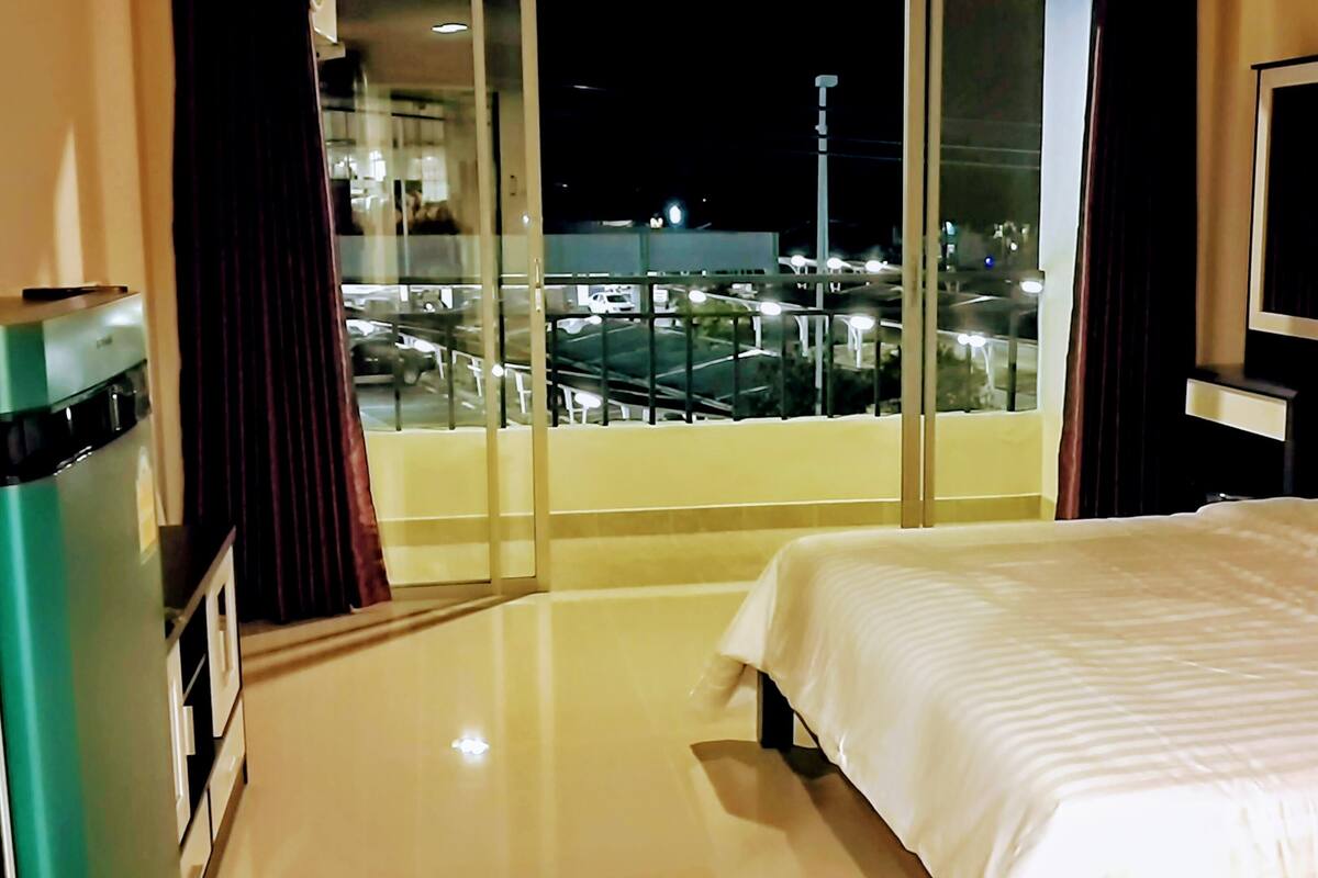 A hotel room with a bed, a minibar, a TV, and a balcony with a view of the city at night.