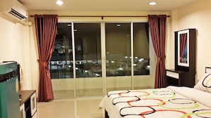 A hotel room with a bed, a TV, a desk, and a sliding glass door to the balcony. - Santa Place (Pattaya)