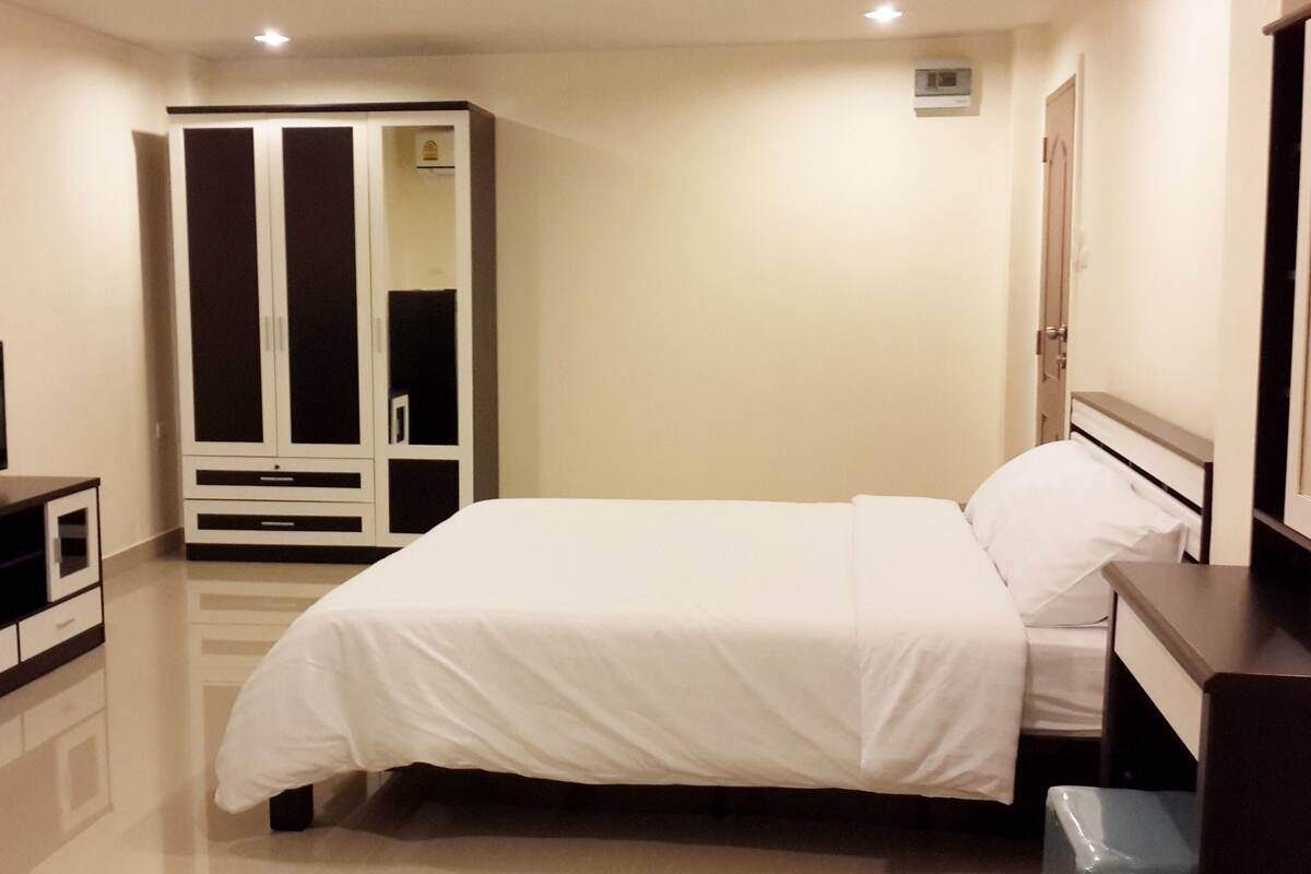 A bedroom with a bed, a wardrobe, a television, and a trash bin.