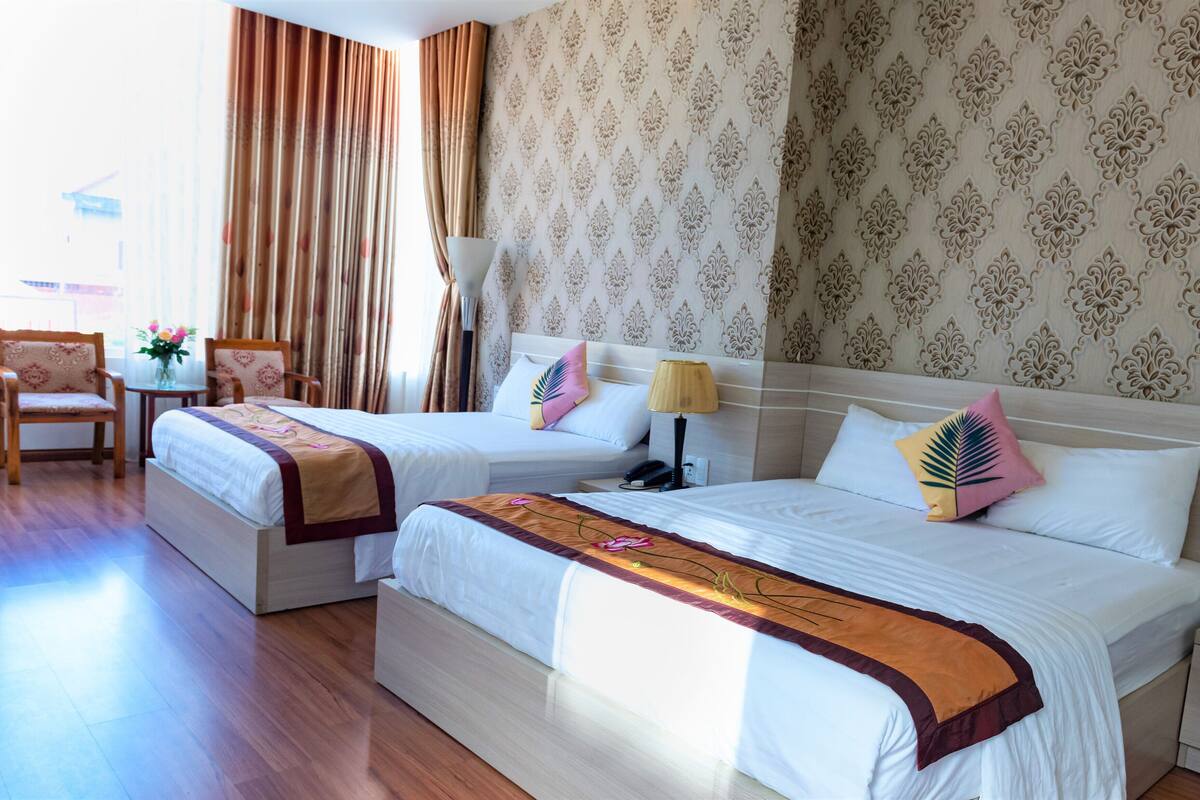Habitación de hotel con dos camas, un escritorio, una silla y un ventanal con cortinas.