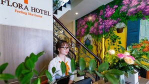 A hotel reception area with a staircase, a sign reading "FLORA HOTEL Feeling like home", and a wall mural of flowers. - Flora Hotel Hue (Hue)