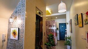 A hallway with patterned walls, a decorative plant, a hanging light fixture, and framed artwork on the wall. - Flora Hotel Hue (Hue)