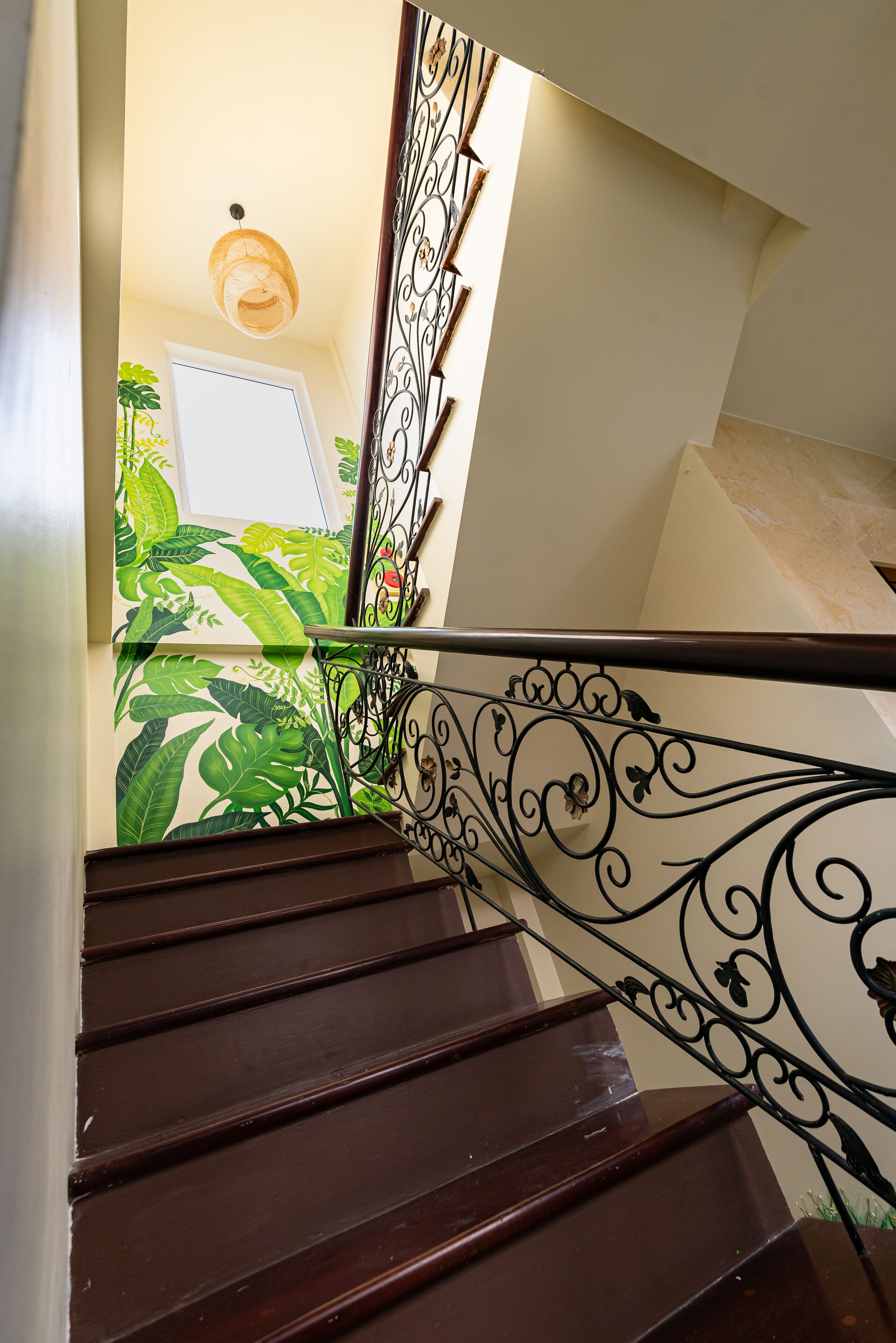 Un escalier en bois, agrémenté de rampes noires décorées, et un mur orné d’un motif de feuilles tropicales.
