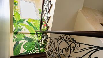 A wooden staircase with ornate black railings and a wall with a tropical leaf pattern.