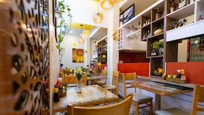 A restaurant with wooden chairs and tables, a red accent wall, and shelves with bottles and glasses. - Flora Hotel Hue (Hue)