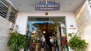 The entrance of Flora Hotel with a glass door, two potted plants on either side, and a sign above the door. - Flora Hotel Hue (Hue)