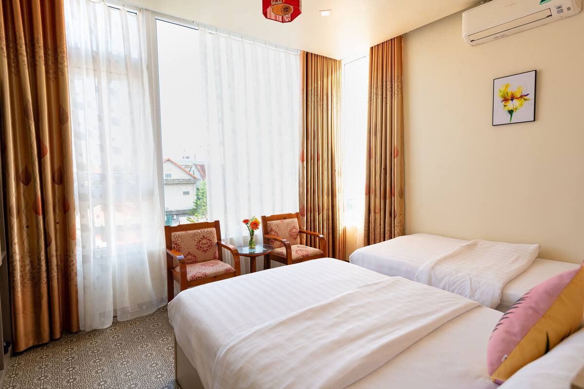 Una habitación de hotel con dos camas, una pequeña mesa con sillas y un ventanal con cortinas.