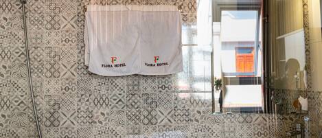 A bathroom with patterned tiles, a white towel with 'Flora Hotel' branding, a sink, and a shower.