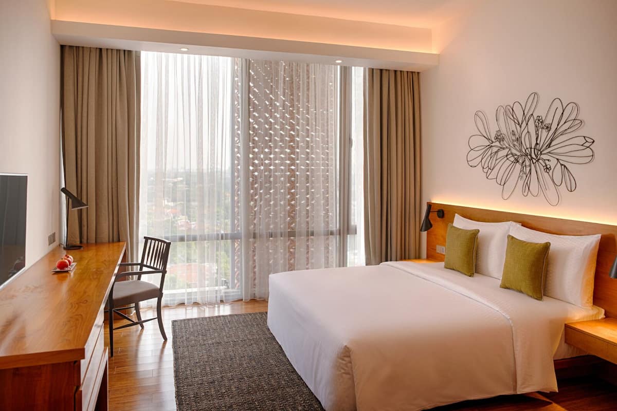 Une chambre d’hôtel avec un grand lit, un bureau, une chaise, une vue par la fenêtre avec des rideaux et une œuvre d’art murale.