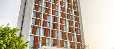 A tall hotel with a modern design, featuring a prominent entrance and a parking area.