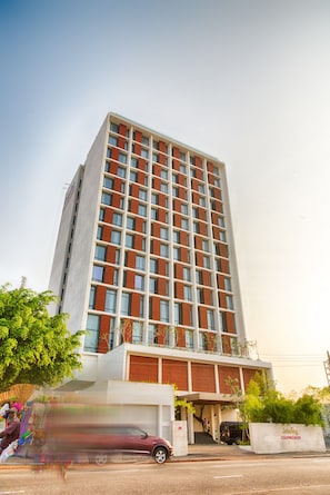 A tall hotel with a modern design, featuring a prominent entrance and a parking area.
