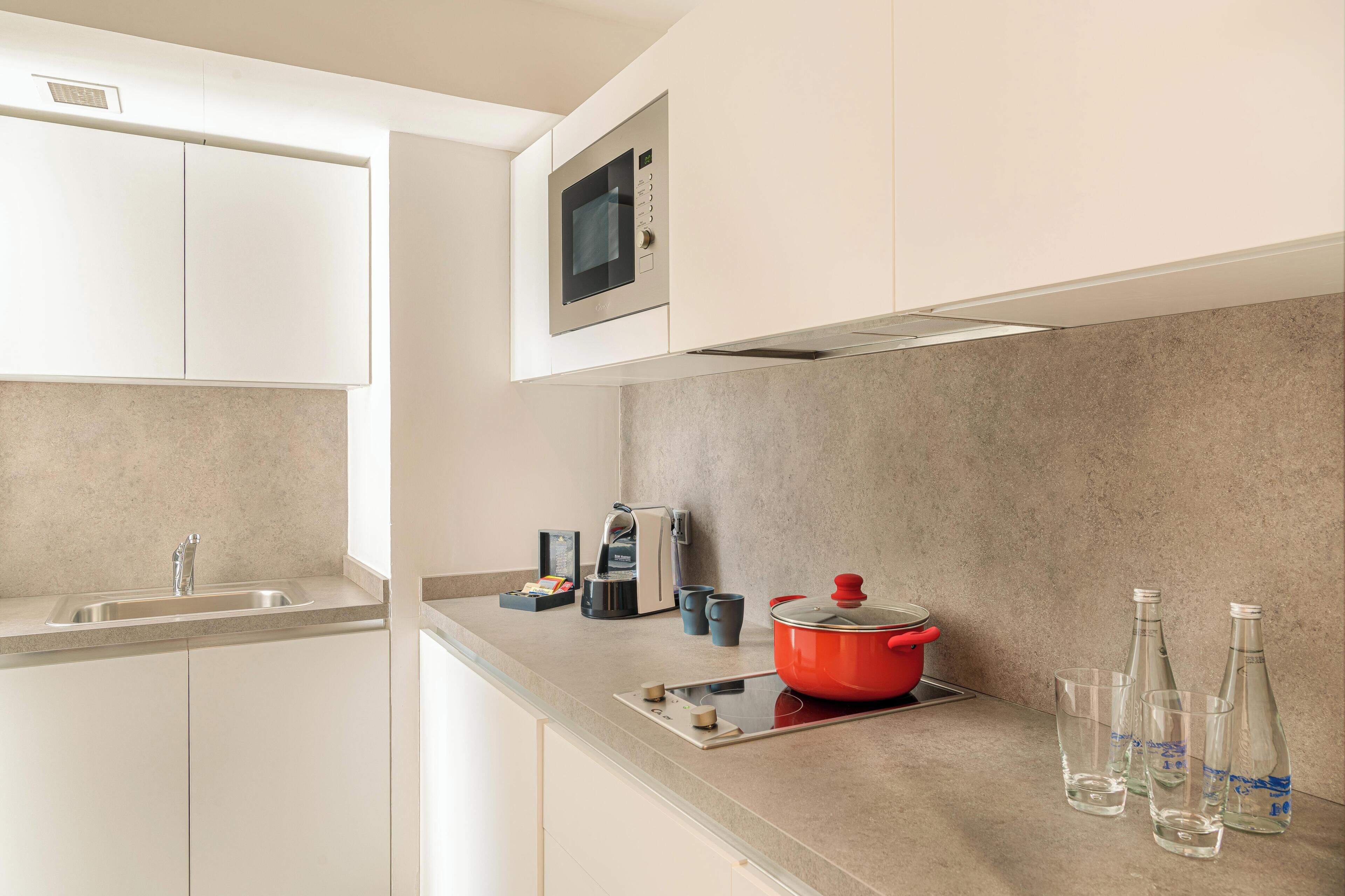 Una cocina moderna con microondas, cafetera, una olla roja y varios vasos sobre la encimera.