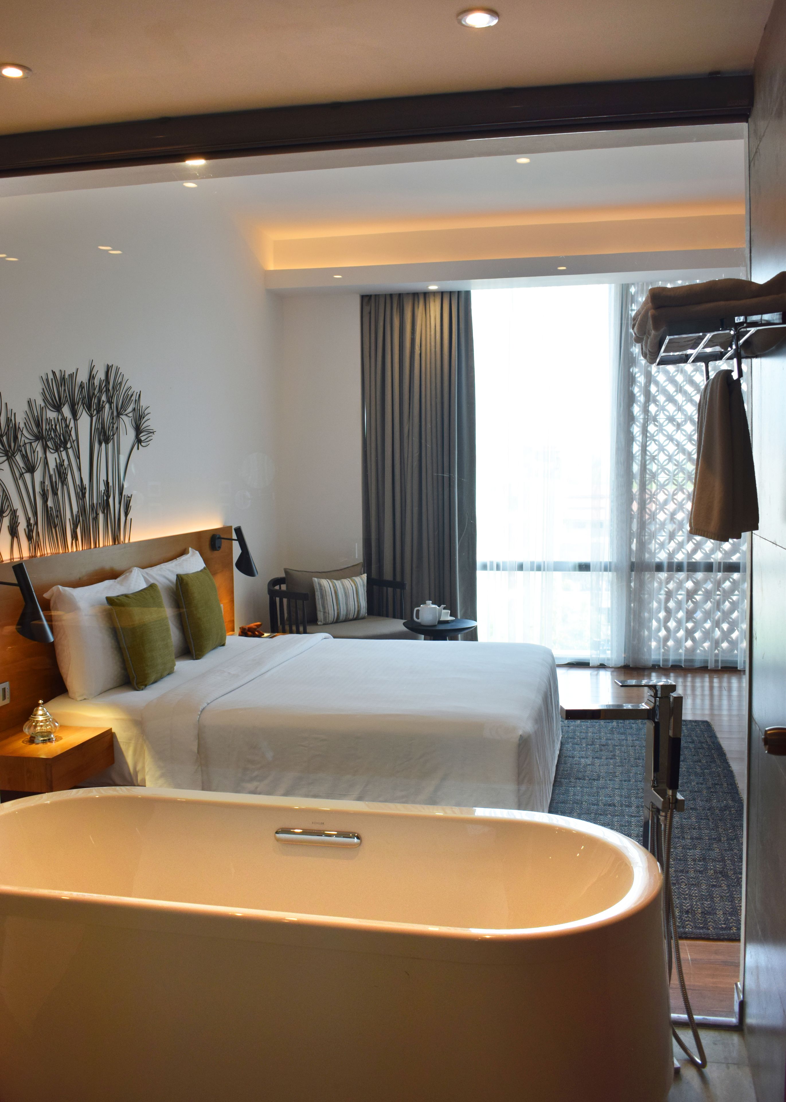 Ein modernes Hotelzimmer mit einem großen Bett, einer separaten Sitzecke, einer Badewanne und Blick durch leichte Vorhänge.
