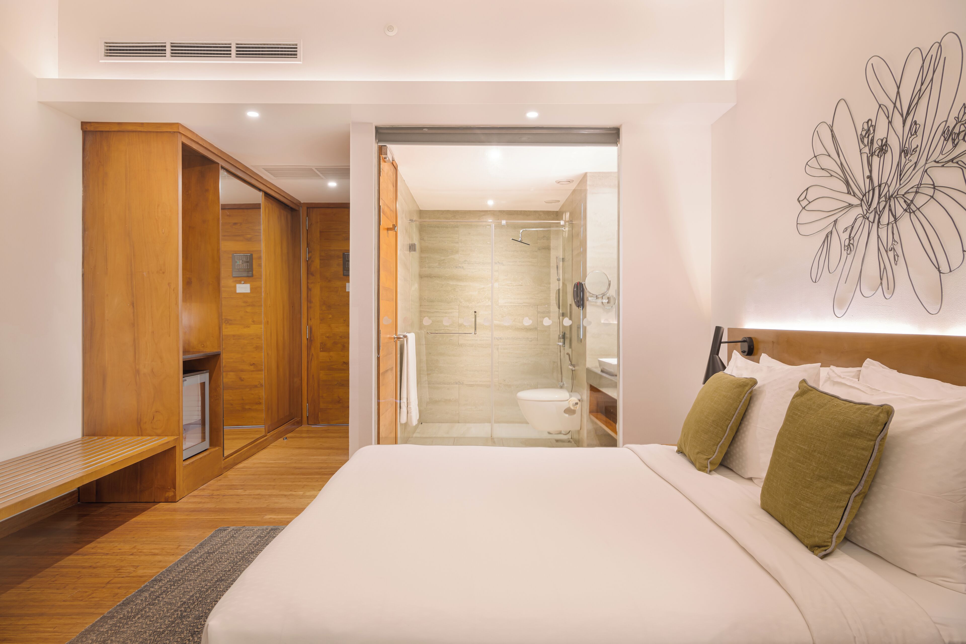 A modern hotel room with a large bed, wooden wardrobe, and a glass-enclosed shower area.