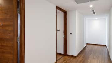 Un pasillo con suelo de madera y paredes blancas, con una puerta de madera a la izquierda y otra al final.