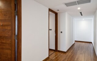 A hallway with wooden flooring and white walls, featuring a wooden door on the left and a door at the end.