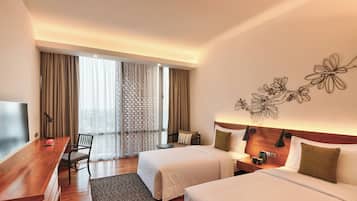 A hotel room with two beds, a desk, a chair, a TV, and a window with curtains.