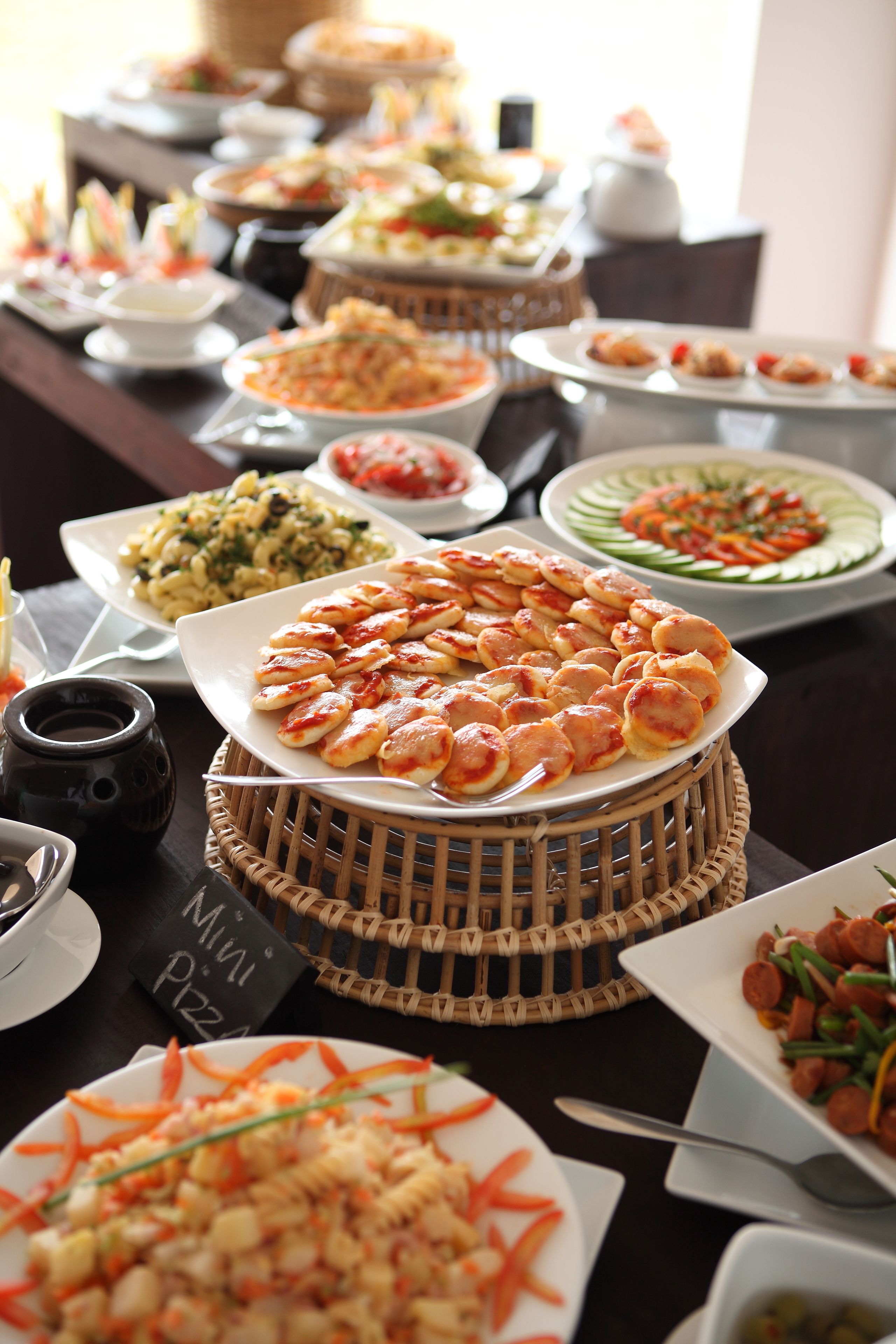 Une table de buffet proposant divers plats, notamment des pâtes, des salades et une assiette de mini-pizzas.