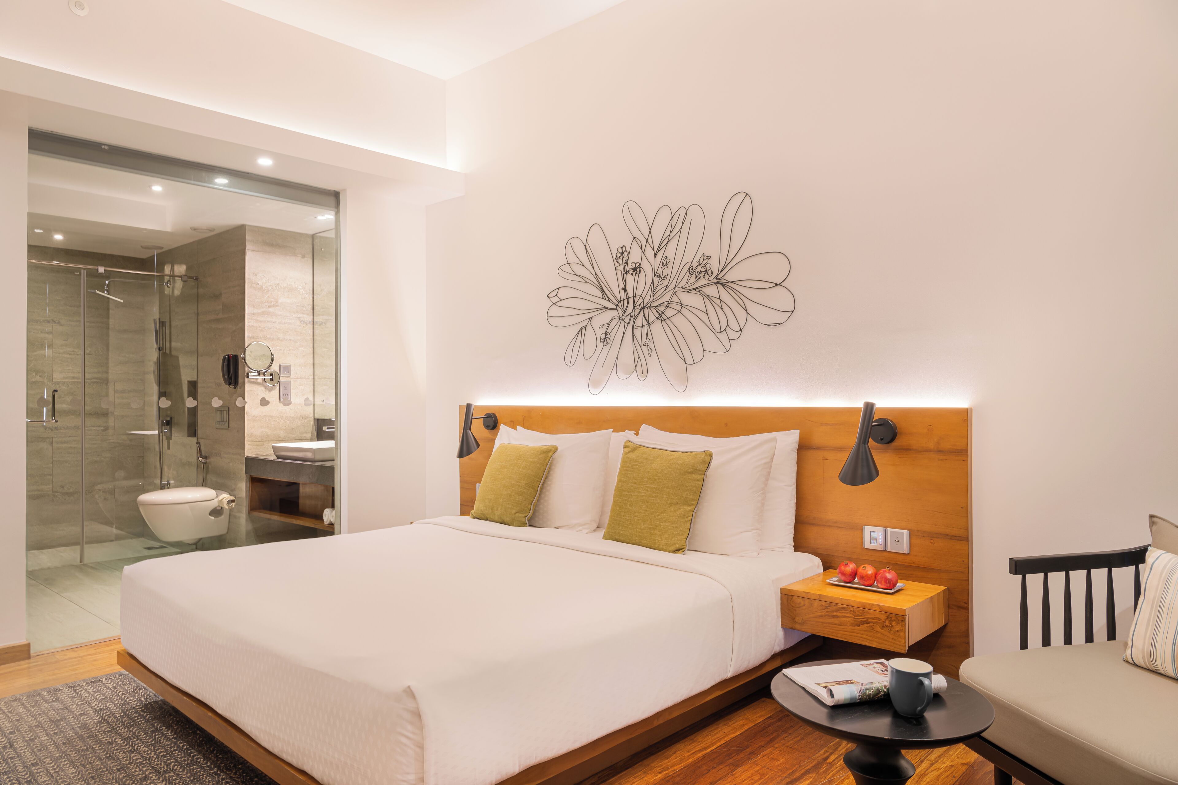 Una habitación de hotel moderna con una cama grande, una mesita de noche con lámpara, una pequeña mesa con una taza y una silla.